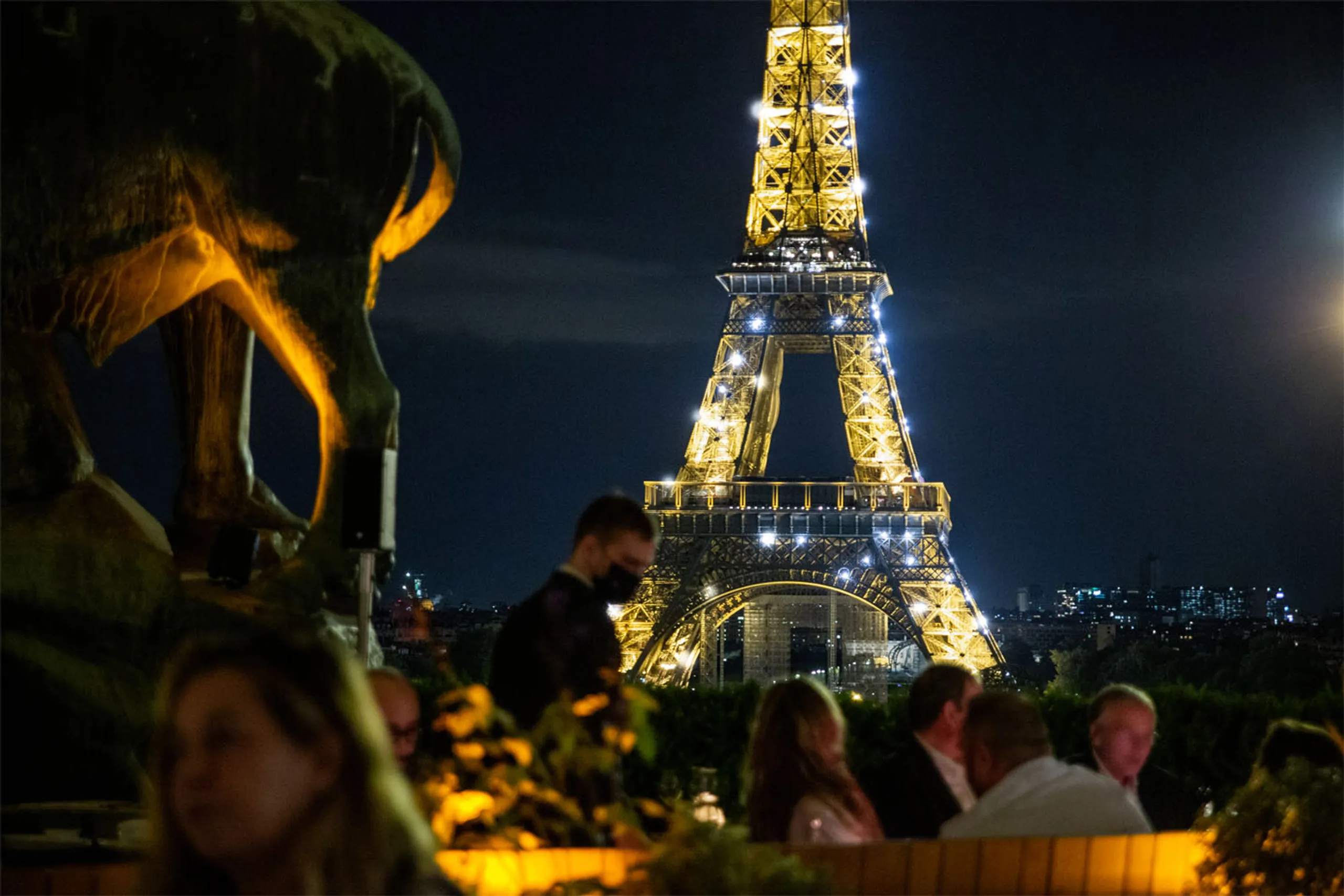 Image représentant la terrasse du Café de l'Homme de nuit devant la Tour Eiffel scintillante.