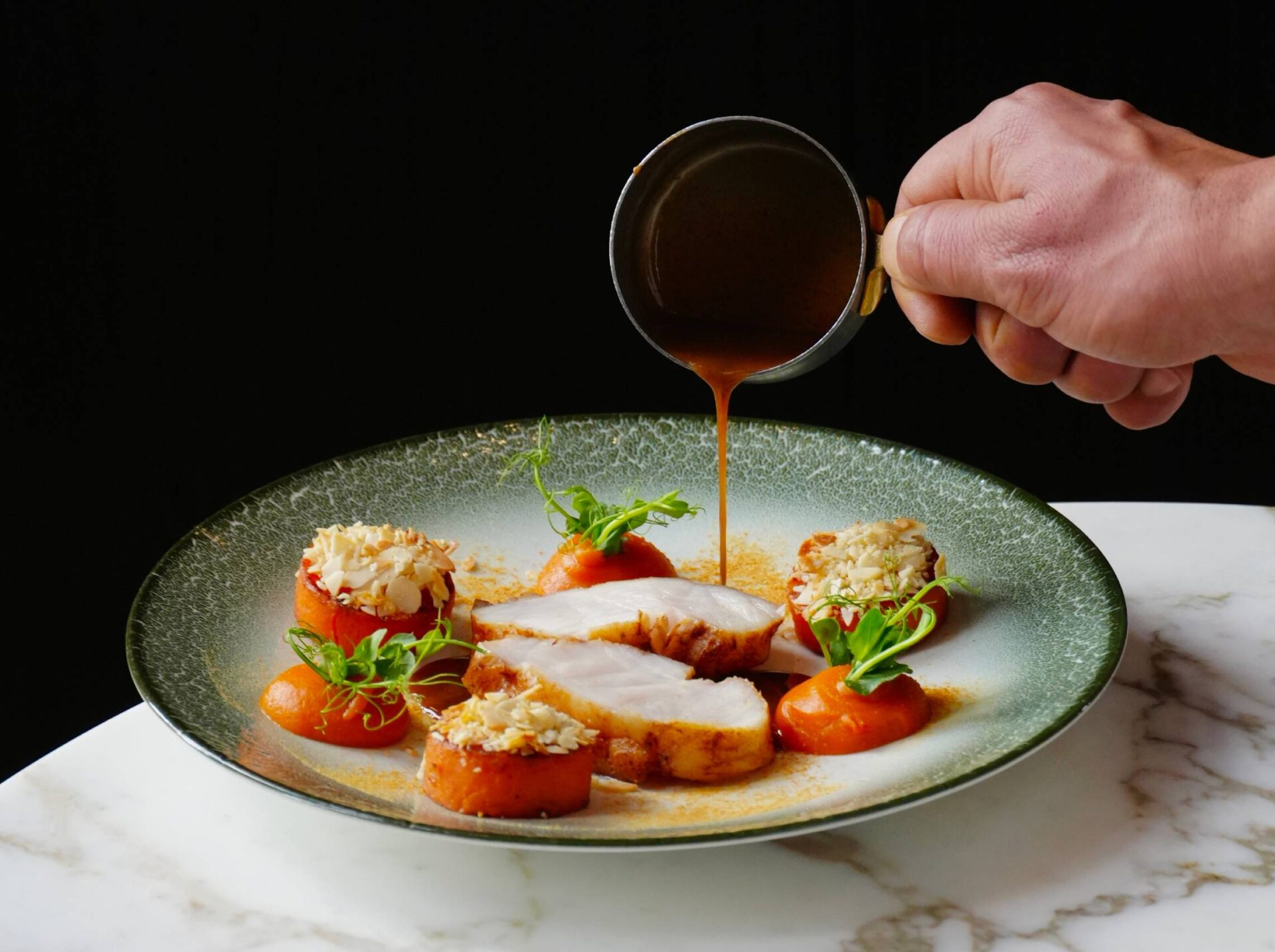 A signature dish being sauced at the moment of service